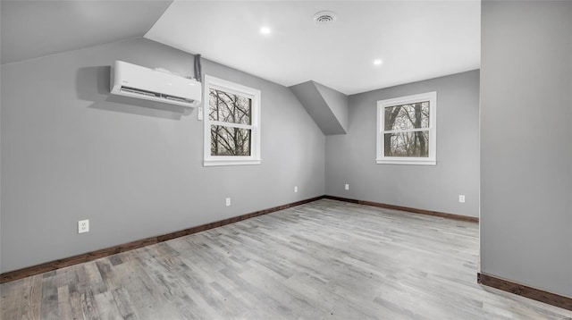 bonus room with lofted ceiling, a wall mounted air conditioner, a wealth of natural light, and light wood-type flooring