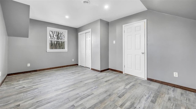 unfurnished bedroom featuring lofted ceiling, a closet, and light wood-type flooring