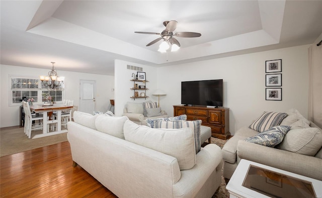 living room with a raised ceiling, hardwood / wood-style flooring, and ceiling fan with notable chandelier