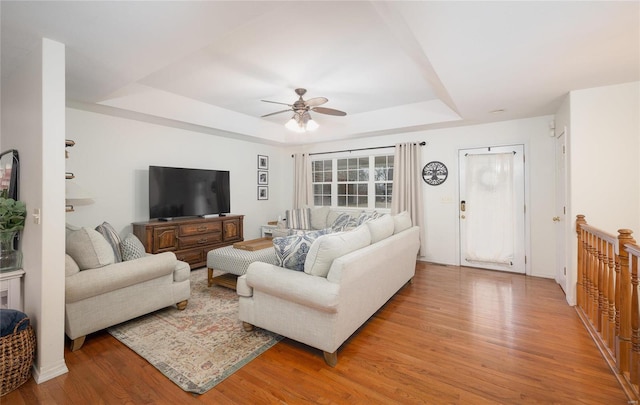 living room with light hardwood / wood-style floors, a raised ceiling, and ceiling fan