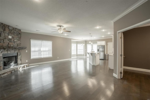 unfurnished living room with a fireplace, ornamental molding, ceiling fan, dark wood-type flooring, and a textured ceiling