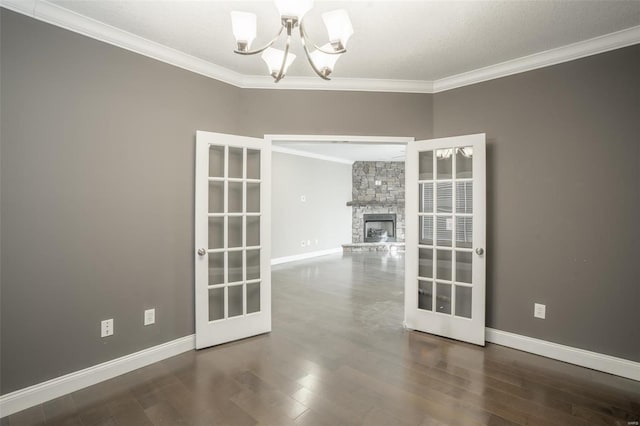 empty room with french doors, a stone fireplace, crown molding, dark hardwood / wood-style floors, and a notable chandelier