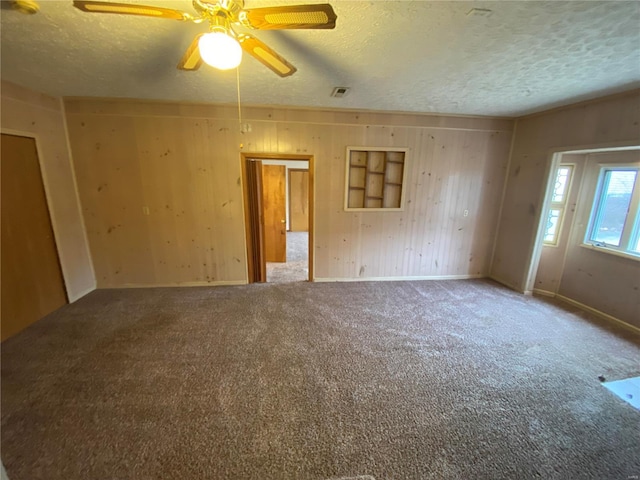 spare room with ceiling fan, carpet flooring, wooden walls, and a textured ceiling