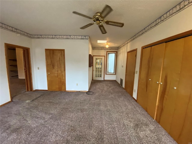 unfurnished bedroom featuring ceiling fan, two closets, a textured ceiling, and dark colored carpet