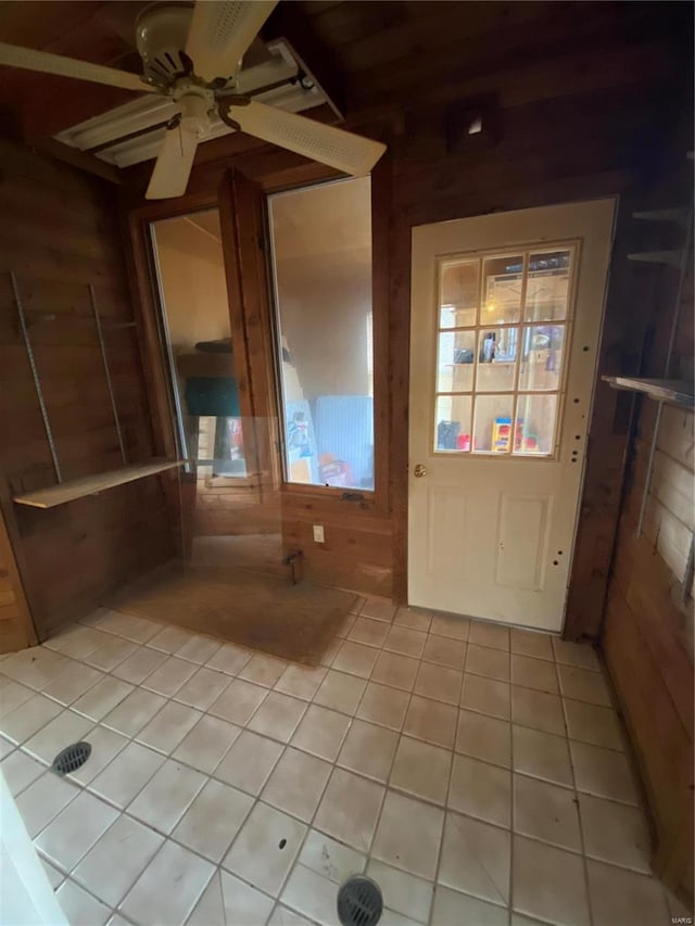 doorway with light tile patterned floors, ceiling fan, and wood walls