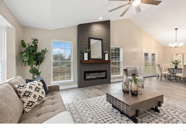 living room featuring a large fireplace, ceiling fan with notable chandelier, high vaulted ceiling, and light hardwood / wood-style flooring