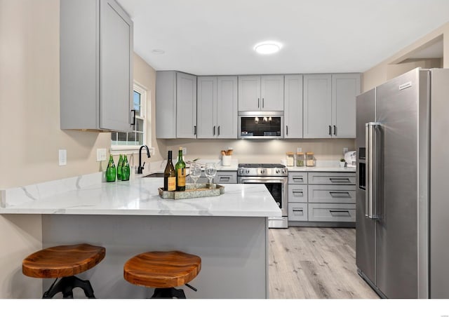 kitchen with sink, gray cabinetry, appliances with stainless steel finishes, a kitchen breakfast bar, and kitchen peninsula