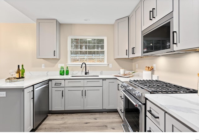 kitchen with gray cabinetry, sink, light stone countertops, and appliances with stainless steel finishes