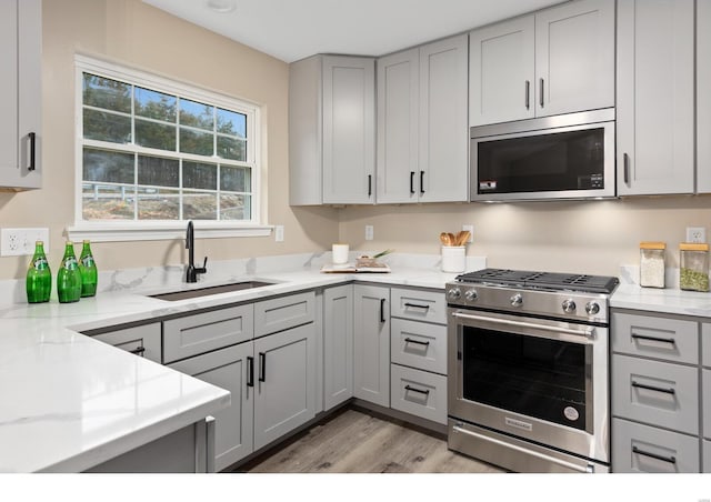 kitchen with appliances with stainless steel finishes, sink, gray cabinetry, light stone countertops, and light wood-type flooring