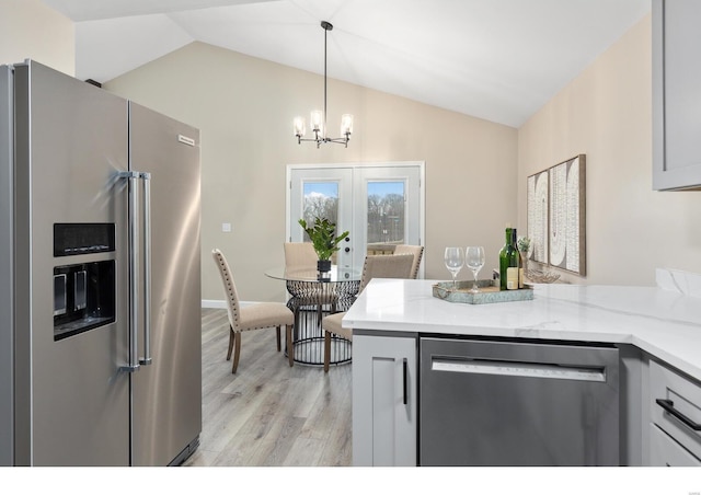 kitchen with pendant lighting, lofted ceiling, appliances with stainless steel finishes, and light stone countertops