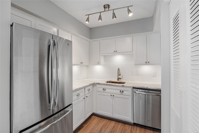 kitchen featuring sink, stainless steel appliances, light stone counters, white cabinets, and light wood-type flooring