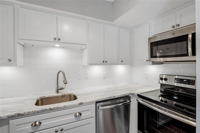 kitchen featuring light stone counters, stainless steel appliances, sink, and white cabinets