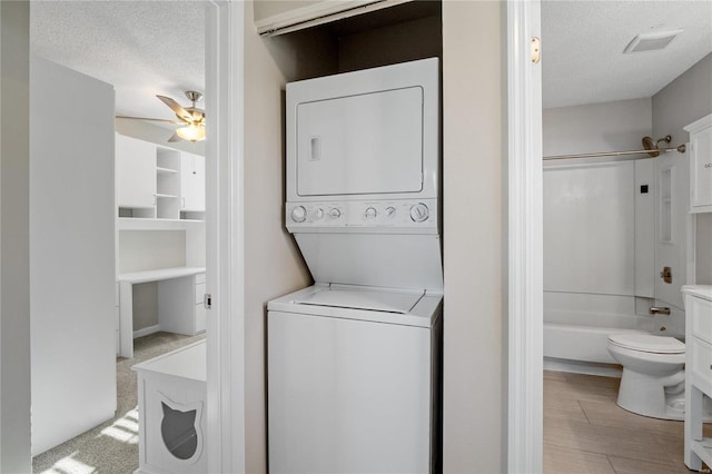 washroom featuring stacked washer / drying machine, a textured ceiling, and ceiling fan