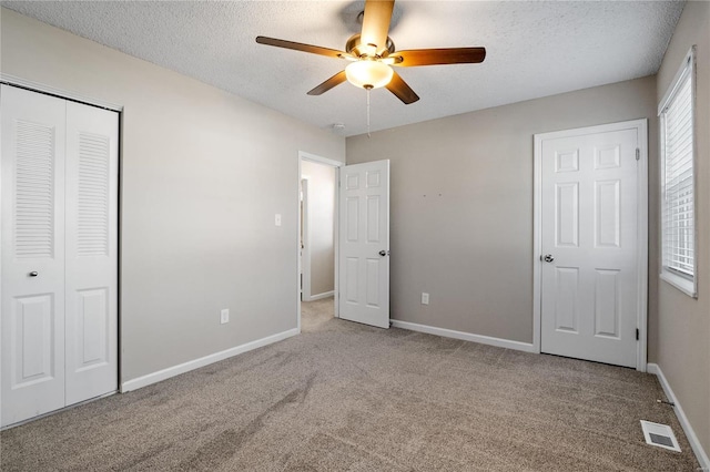 unfurnished bedroom featuring ceiling fan, a closet, light carpet, and a textured ceiling