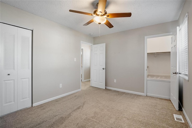 unfurnished bedroom with ceiling fan, light colored carpet, a closet, and a textured ceiling