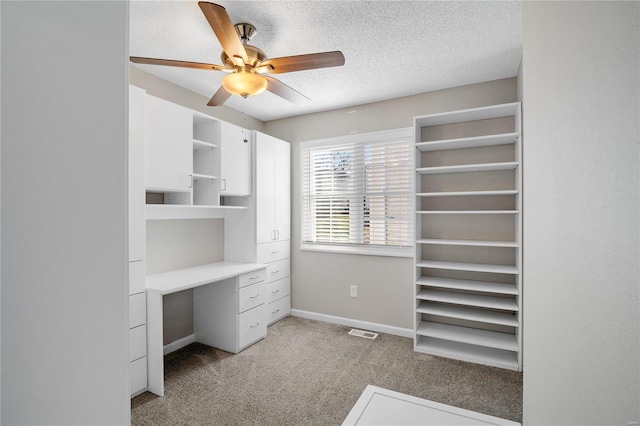 interior space with light carpet, ceiling fan, built in desk, and a textured ceiling