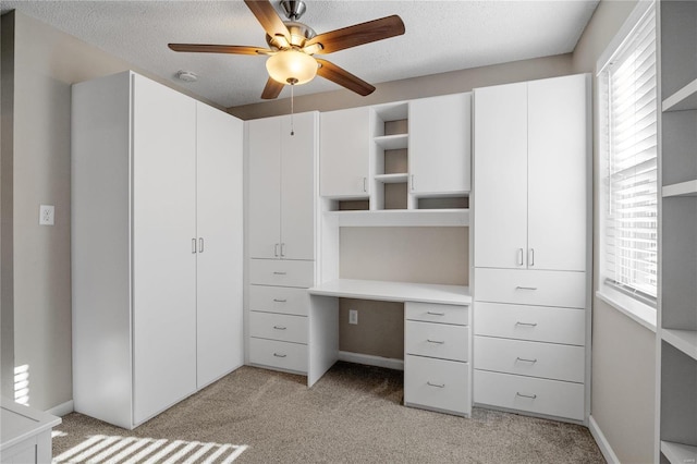 unfurnished office with ceiling fan, light colored carpet, built in desk, and a textured ceiling