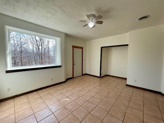 tiled empty room with ceiling fan and a textured ceiling