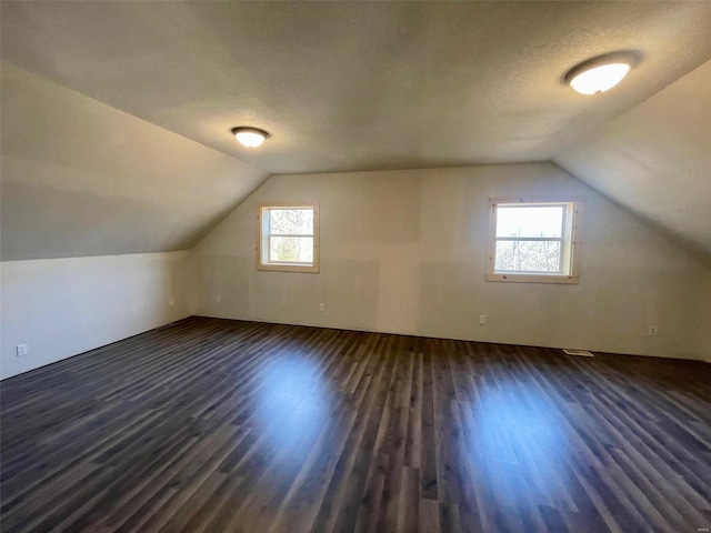 bonus room with lofted ceiling, dark wood-type flooring, and a textured ceiling