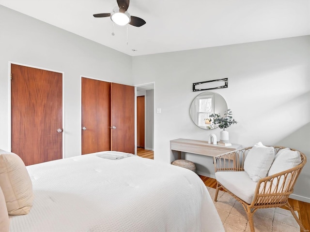 bedroom featuring lofted ceiling, two closets, ceiling fan, and light wood-type flooring