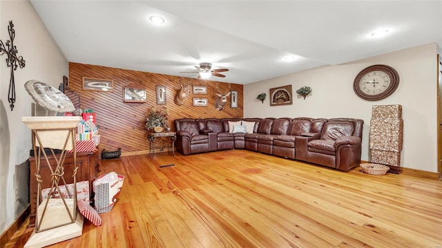 living room featuring ceiling fan, wood-type flooring, and wooden walls