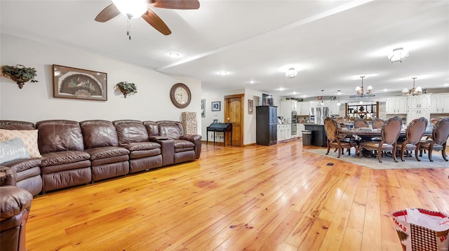 living room with ceiling fan with notable chandelier and light hardwood / wood-style flooring