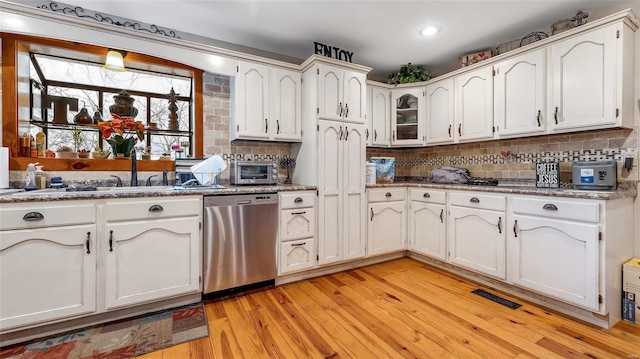 kitchen with light hardwood / wood-style flooring, backsplash, white cabinets, stainless steel dishwasher, and dark stone counters