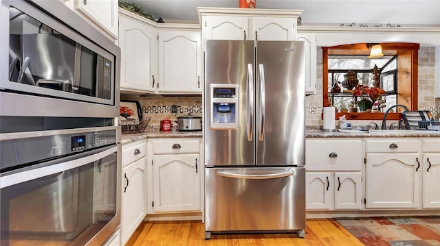 kitchen with sink, white cabinets, dark stone counters, stainless steel appliances, and light hardwood / wood-style flooring