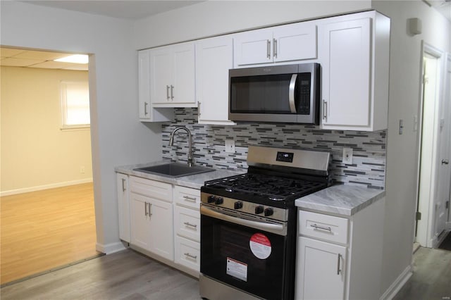 kitchen with stainless steel appliances, light countertops, light wood-type flooring, white cabinetry, and a sink