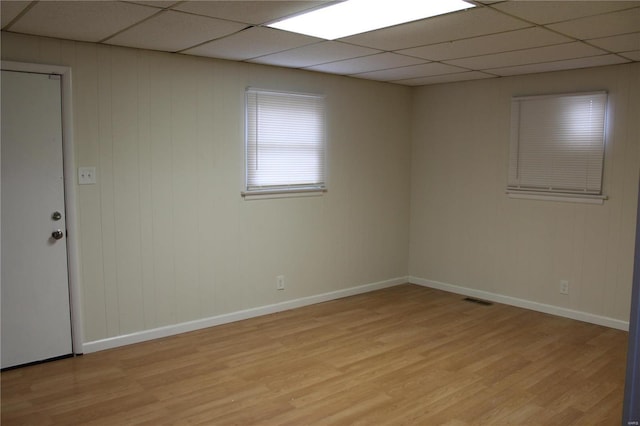 unfurnished room with a paneled ceiling, light wood-style flooring, visible vents, and baseboards