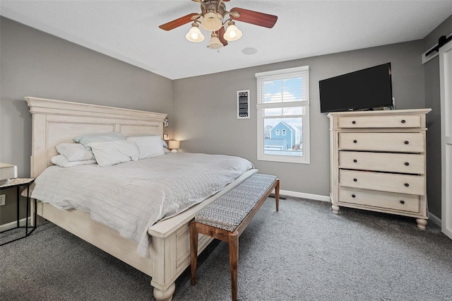 bedroom with ceiling fan, a barn door, and dark carpet