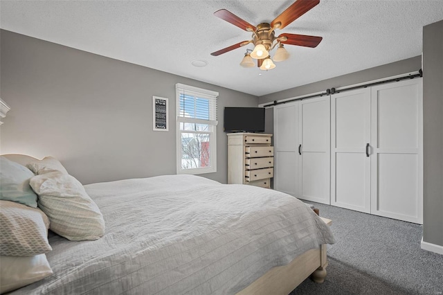 carpeted bedroom with ceiling fan, a barn door, and a textured ceiling