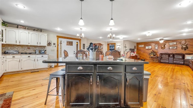 kitchen with white cabinetry, hanging light fixtures, a kitchen island with sink, a kitchen breakfast bar, and light wood-type flooring