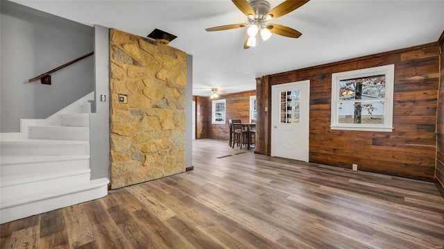 unfurnished living room featuring hardwood / wood-style flooring, ceiling fan, and wooden walls