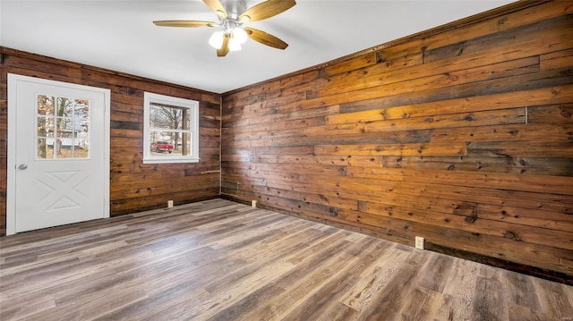 spare room featuring hardwood / wood-style flooring, wooden walls, and ceiling fan