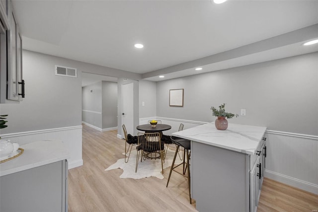 kitchen with visible vents, wainscoting, light stone countertops, gray cabinets, and light wood-type flooring