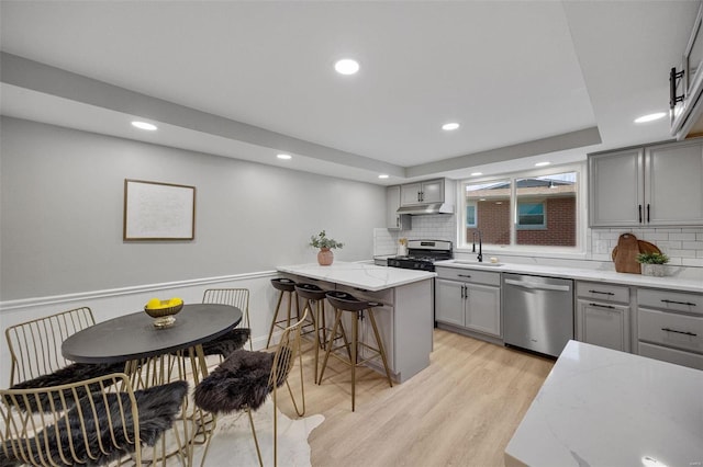 kitchen with light wood finished floors, a kitchen breakfast bar, gray cabinets, stainless steel appliances, and a sink