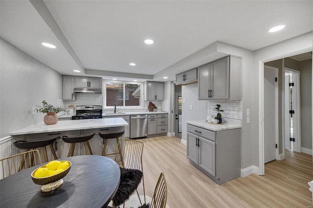 kitchen with light wood-style flooring, under cabinet range hood, stainless steel appliances, a sink, and gray cabinets