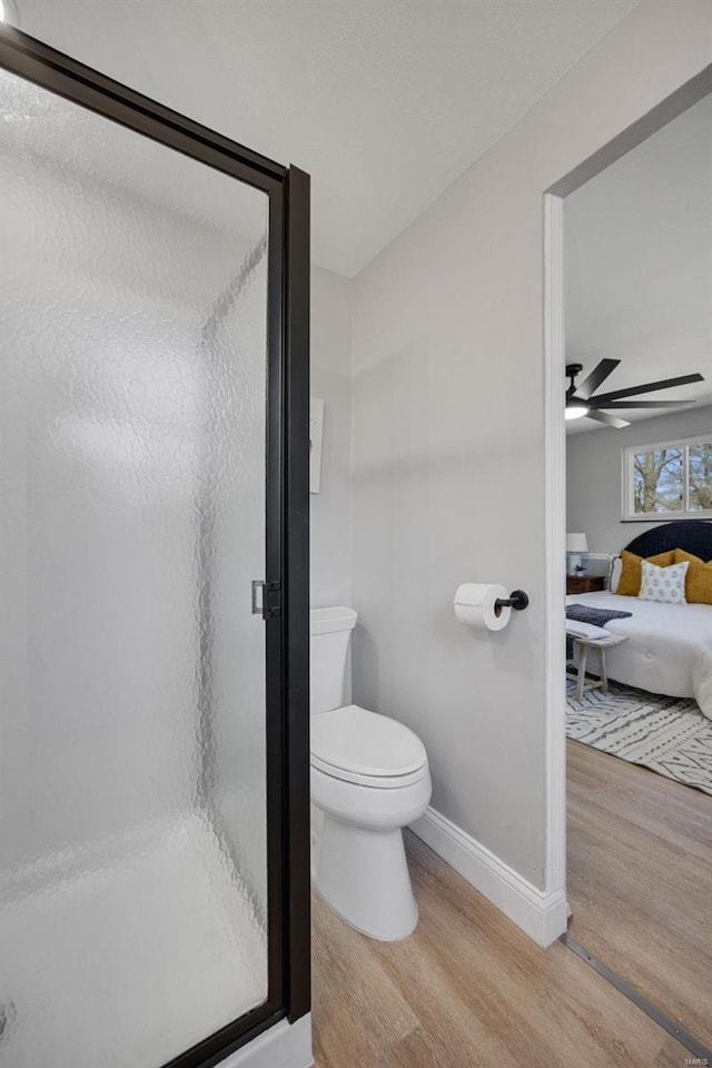 ensuite bathroom with toilet, wood finished floors, a ceiling fan, baseboards, and a shower stall