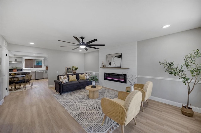 living room featuring a large fireplace, baseboards, light wood finished floors, and recessed lighting