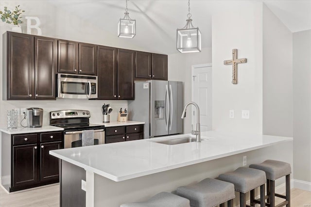 kitchen with appliances with stainless steel finishes, decorative light fixtures, sink, a breakfast bar area, and kitchen peninsula