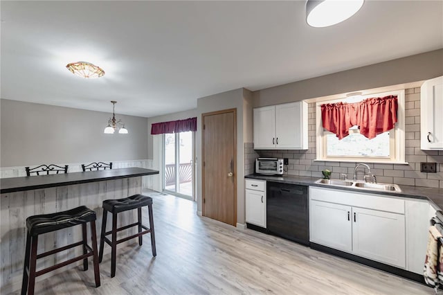 kitchen featuring a breakfast bar, sink, hanging light fixtures, black dishwasher, and white cabinets