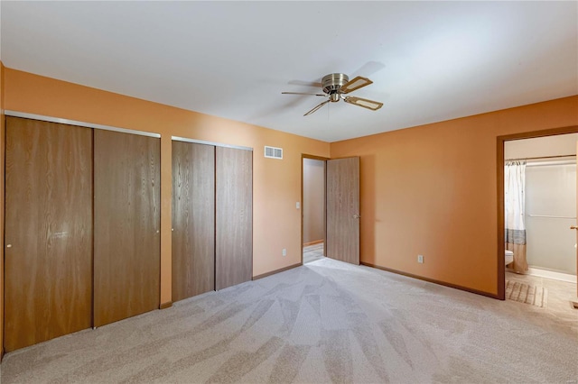 unfurnished bedroom with connected bathroom, two closets, light colored carpet, and ceiling fan