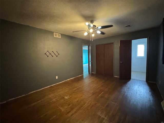 unfurnished bedroom with ceiling fan, dark wood-type flooring, two closets, and a textured ceiling