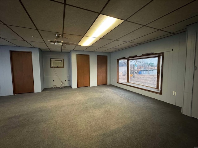 carpeted spare room with a wall unit AC, a drop ceiling, and ceiling fan