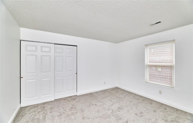 unfurnished bedroom with light carpet, a textured ceiling, and a closet