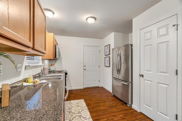 kitchen with sink, dark stone countertops, stainless steel appliances, dark wood-type flooring, and a textured ceiling