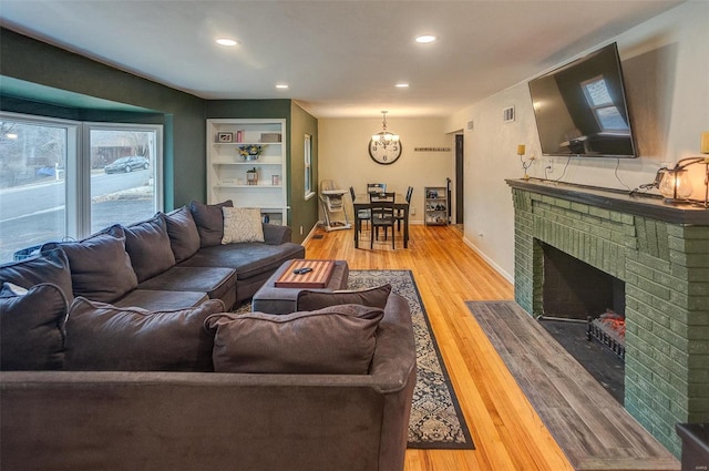 living room with a brick fireplace, built in shelves, and light hardwood / wood-style flooring