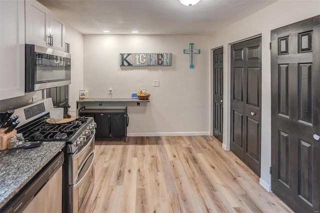 kitchen with stainless steel appliances, white cabinetry, dark stone countertops, and light hardwood / wood-style floors