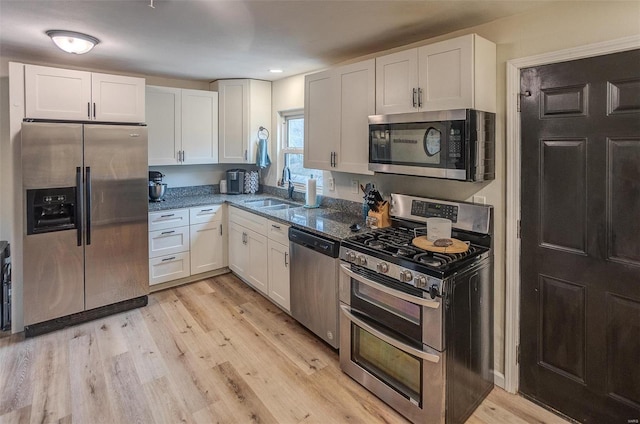 kitchen with appliances with stainless steel finishes, sink, dark stone counters, and white cabinets